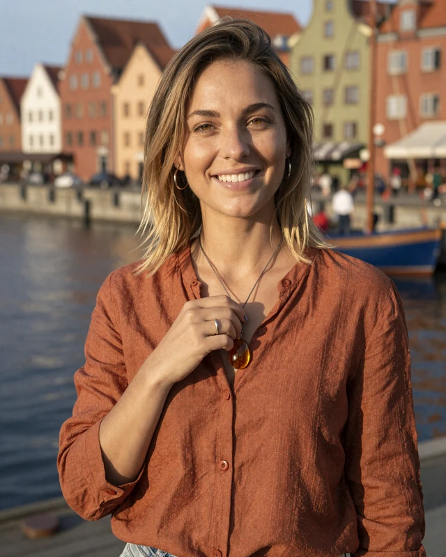 Zofia from Gdańsk in rust linen blouse holding an amber pendant by the harbor